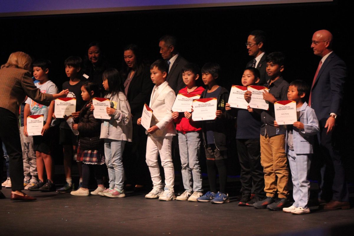 Students stand on stage as they are honored for their proficiency in English